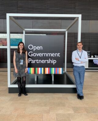 Emily and Andrew in front of a large OGP sign